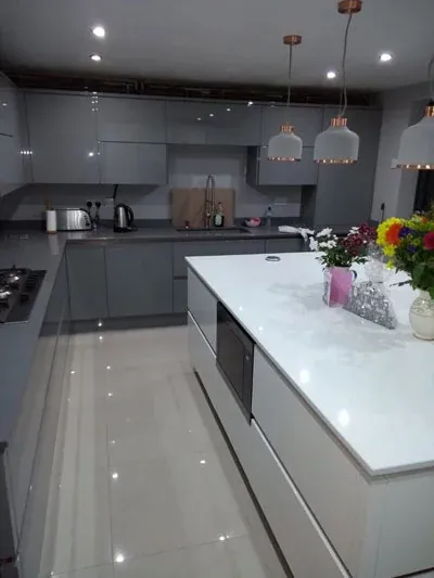 Grey gloss L-shaped kitchen with a white quartz island, copper pendant lights and a gloss tiled floor