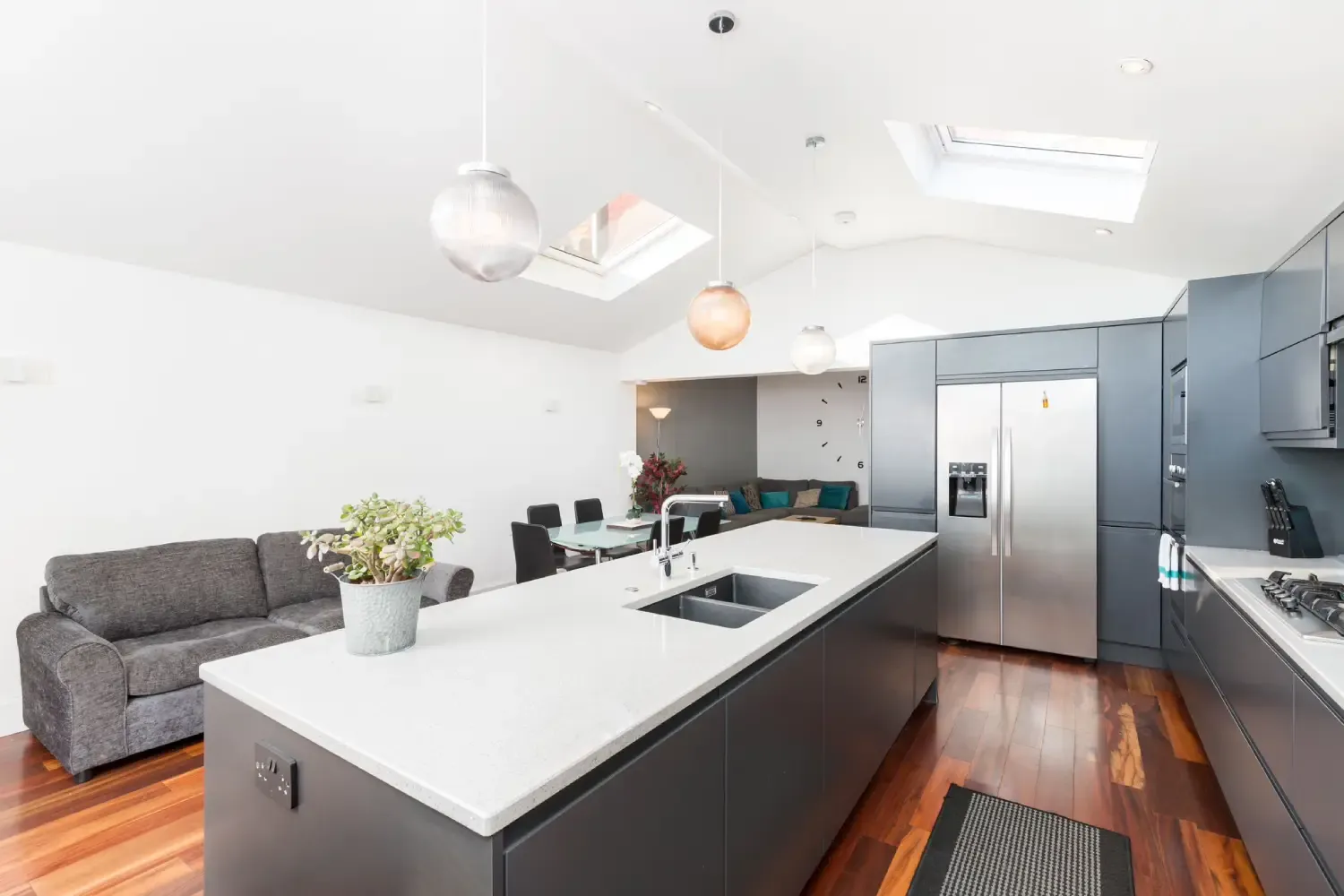 Open-plan slate handleless kitchen with a white quartz island under skylights, with a sofa and dining table beyond