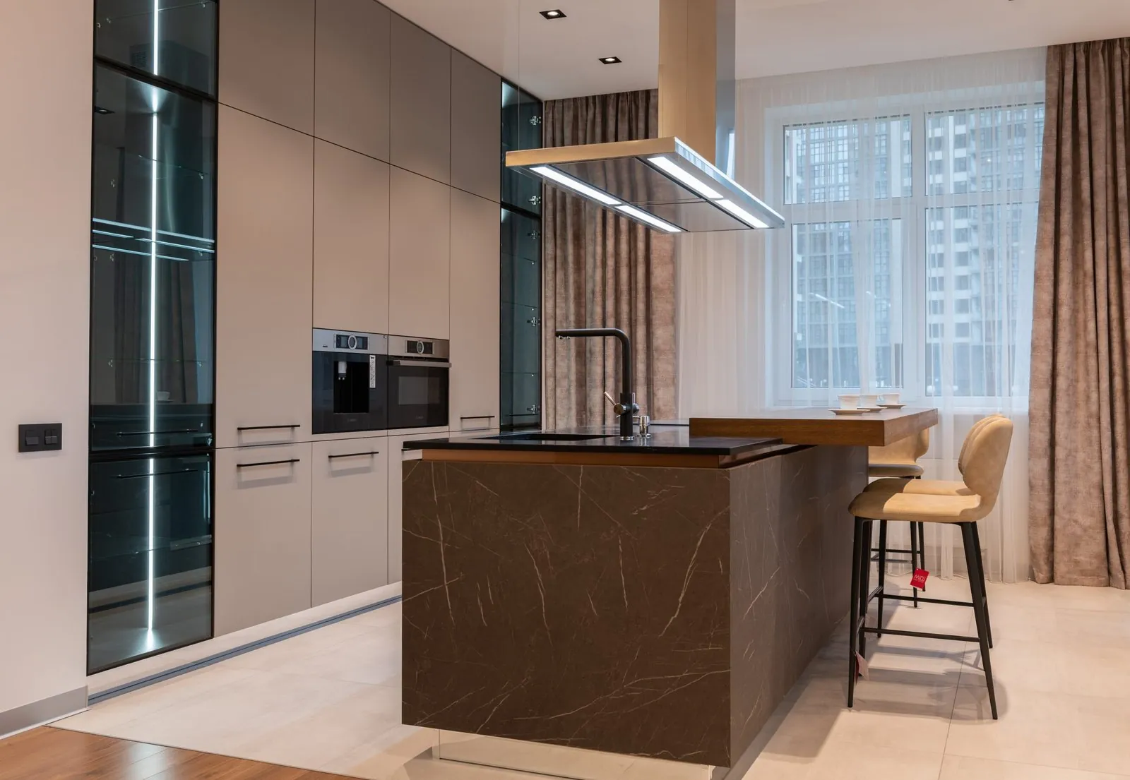 Cashmere tall units, brown marble-effect island with an oak bar top, LED-lit glass larder and ceiling extractor