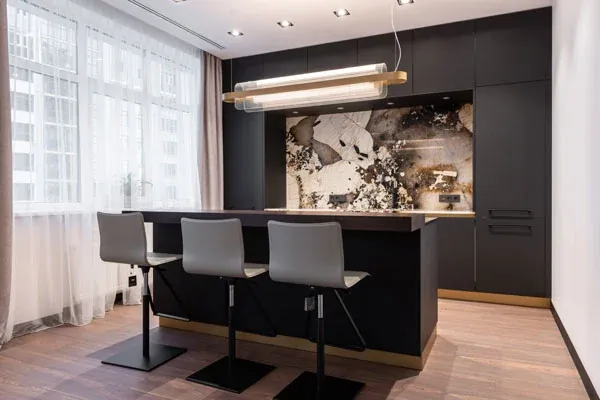 Matt black kitchen with a marble slab feature wall, a brass linear pendant and grey bar stools