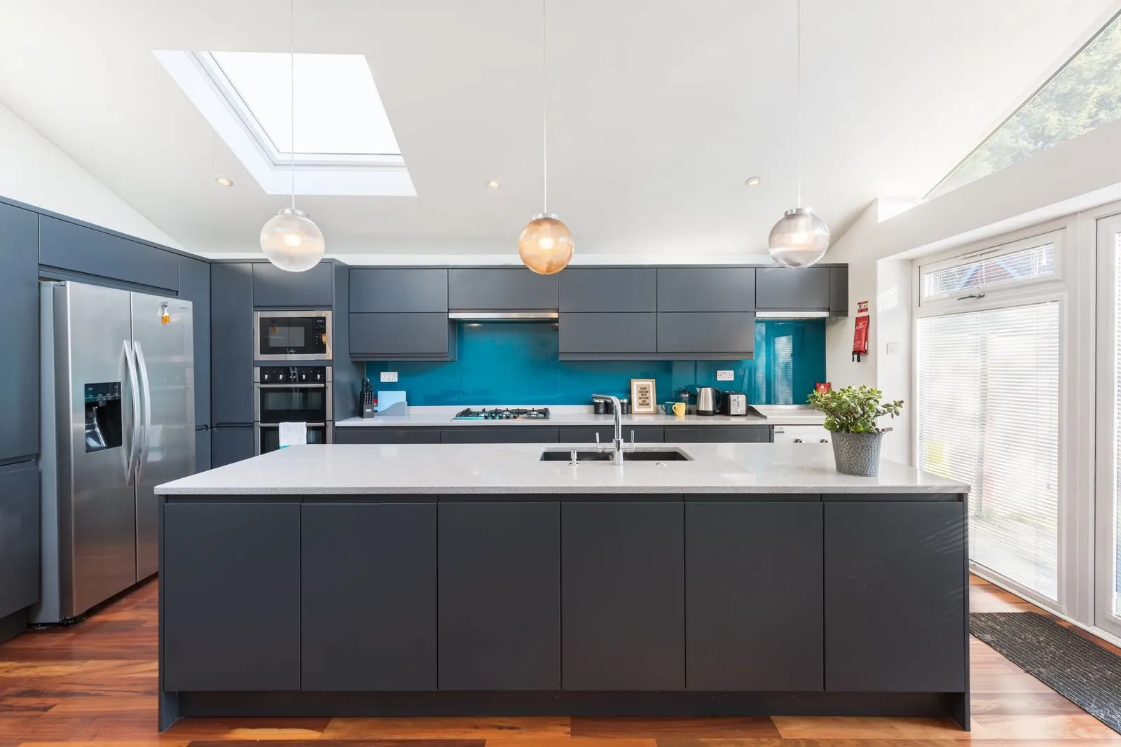 Slate grey handleless kitchen with a teal glass splashback, white quartz island and wood floor