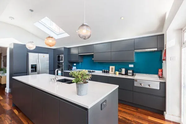 The slate grey handleless kitchen with the teal glass splashback, seen from the far end of the island